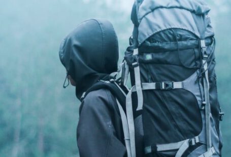 Backpacking - Man Wearing Black Hoodie Carries Black and Gray Backpacker Near Trees during Foggy Weather