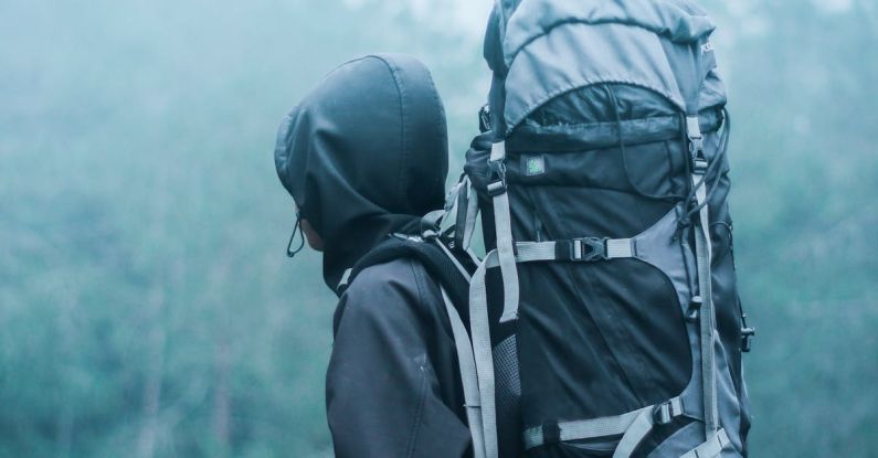 Backpacking - Man Wearing Black Hoodie Carries Black and Gray Backpacker Near Trees during Foggy Weather