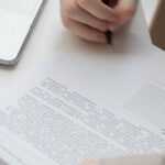 Signature Style - Faceless male worker with paper document near laptop on desk