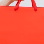 Clearance Sales - Crop unrecognizable female showing red paper shopping bag in hand against white wall