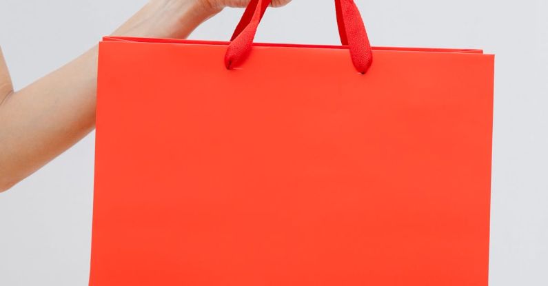 Clearance Sales - Crop unrecognizable female showing red paper shopping bag in hand against white wall