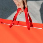 Holiday Sales - High angle of crop anonymous female buyer taking red paper bag with purchase in sunshine