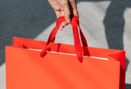 Holiday Sales - High angle of crop anonymous female buyer taking red paper bag with purchase in sunshine