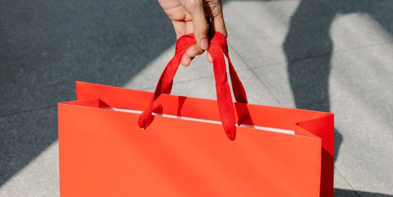 Holiday Sales - High angle of crop anonymous female buyer taking red paper bag with purchase in sunshine