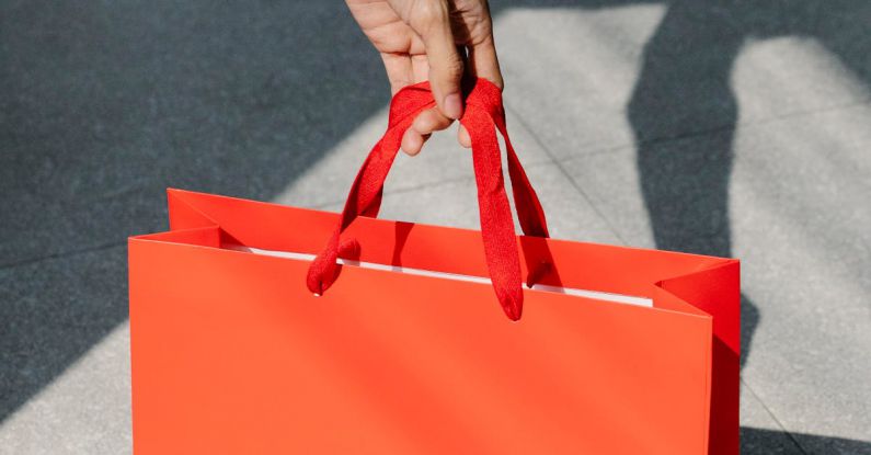 Holiday Sales - High angle of crop anonymous female buyer taking red paper bag with purchase in sunshine