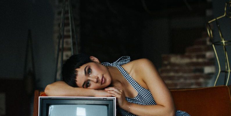 Vintage Designer - Peaceful female wearing overall lying on vintage TV set sitting on seethe in tailor workshop for sale