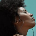 Fitness Fashion - From below side view of young reflective ethnic female model with big earrings and closed eyes under blue sky