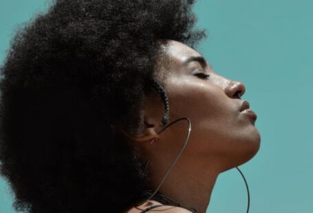 Fitness Fashion - From below side view of young reflective ethnic female model with big earrings and closed eyes under blue sky