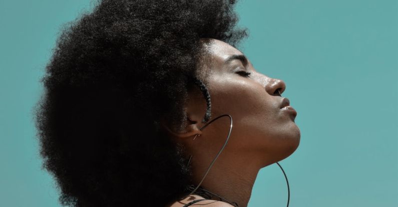 Fitness Fashion - From below side view of young reflective ethnic female model with big earrings and closed eyes under blue sky